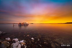 Rays of light burst from the horizon beside the two wrecks settled permanently on the bed of the harbour. Southland, South Island, New Zealand - landscape photography